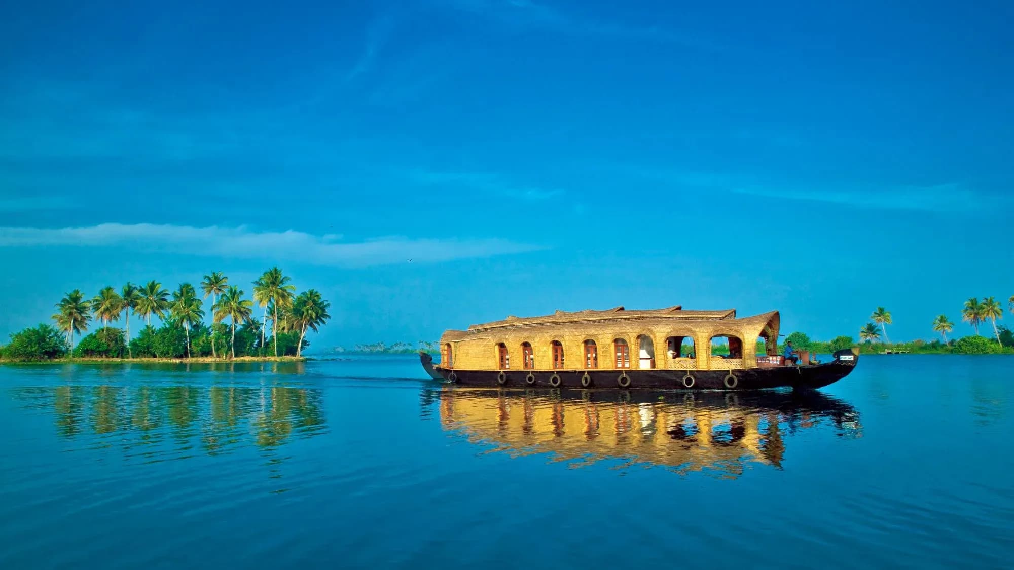 Houseboat cruising on calm backwater with a palm-fringed island and reflections under a blue sky
